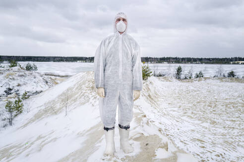 Mann mit Schutzanzug und Maske steht in einer ländlichen Winterlandschaft - EYAF00991