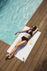 Sinnliche Frau im schwarzen Bikini beim Sonnenbaden am sonnigen Sommerpool - HOXF05445