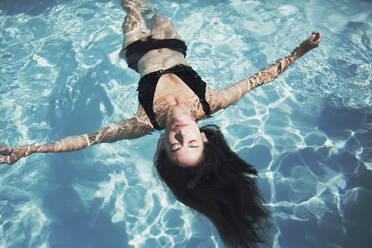 Serene Frau in schwarzem Bikini schwimmt im sonnigen Sommer Schwimmbad - HOXF05448
