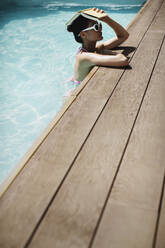 Woman holding book overhead in sunny summer swimming pool - HOXF05455