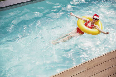 Portrait carefree woman in Santa hat and heart-shape sunglasses swimming with inflatable ring in swimming pool - HOXF05458