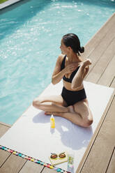 Frau trägt Sonnenschutzmittel am sonnigen Sommerpool auf - HOXF05480