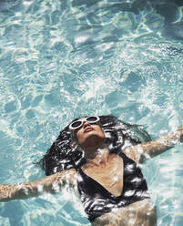 Serene, sensual woman in sunglasses and bikini floating in sunny swimming pool - HOXF05484