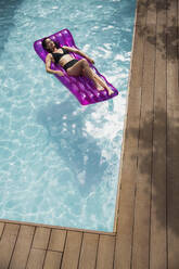 Serene woman relaxing on inflatable raft in swimming pool - HOXF05490