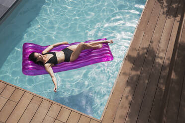 Serene woman relaxing on inflatable raft in sunny summer swimming pool - HOXF05493