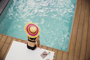 Frau in Sonnenhut und Bikini entspannt am Pool - HOXF05495