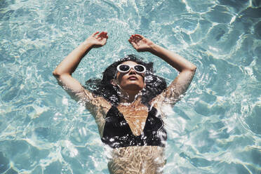 Serene woman floating in sunny summer swimming pool - HOXF05508