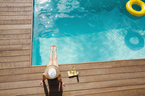 Frau mit Sonnenhut entspannt sich, nimmt ein Sonnenbad am sonnigen Sommerpool, lizenzfreies Stockfoto