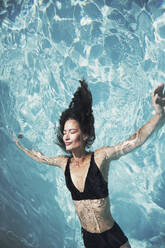 Serene Frau in schwarzem Bikini schwimmt im sonnigen Sommer Schwimmbad - HOXF05514