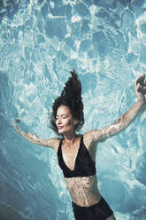 Serene woman in black bikini floating in sunny summer swimming pool - HOXF05514