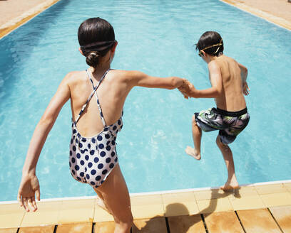 Junge und Mädchen halten sich an den Händen und springen in ein sonniges Sommerschwimmbad - HOXF05518