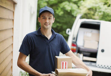 Portrait confident deliveryman with packages at front door - HOXF05524
