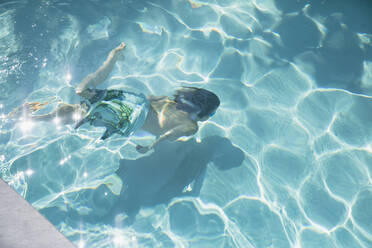 Junge schwimmt unter Wasser im sonnigen Sommerschwimmbad - HOXF05534