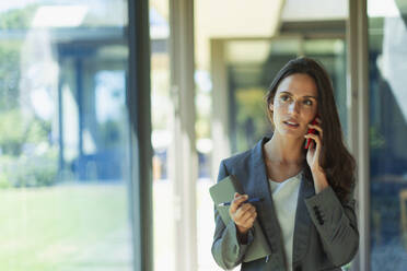 Businesswoman talking on cell phone in corridor - HOXF05539