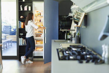 Woman standing at open refrigerator in kitchen - HOXF05544
