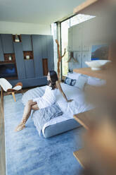 Frau in Handtuch eingewickelt, entspannt auf dem Bett in einem modernen Schlafzimmer - HOXF05568