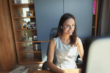 Smiling businesswoman with headset working at computer in home office - HOXF05581