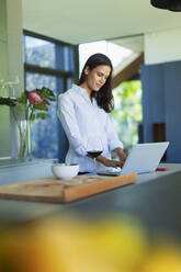 Woman using laptop and drinking red wine in kitchen - HOXF05590