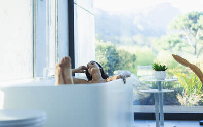 Gelassene Frau entspannt sich in einer Badewanne in einem modernen Badezimmer - HOXF05611
