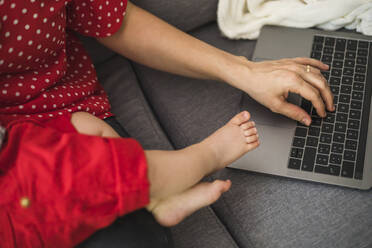 Mutter arbeitet mit Laptop auf dem Sofa, während sie ihren schläfrigen kleinen Jungen hält - FLMF00208