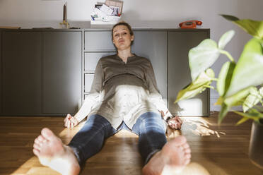 Porträt einer erschöpften schwangeren Frau, die zu Hause auf dem Boden sitzt - MFF05088