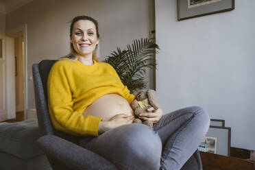 Porträt einer lächelnden schwangeren Frau, die zu Hause auf einem Stuhl sitzt - MFF05091