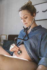 Pregnant woman holding a stethoscope to hear the heartbeat of her baby - MFF05096