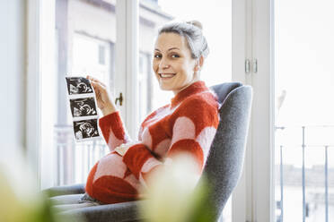 Porträt einer schwangeren Frau, die ein Ultraschallbild zu Hause zeigt - MFF05098