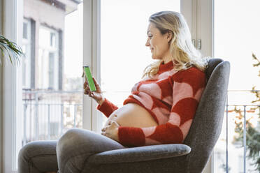 Schwangere Frau schaut auf ihr Handy zu Hause - MFF05100