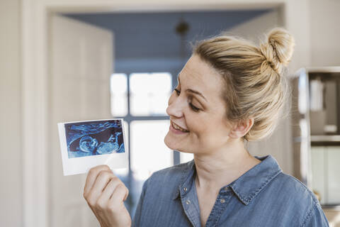 Schwangere Frau hält Ultraschallbild zu Hause, lizenzfreies Stockfoto