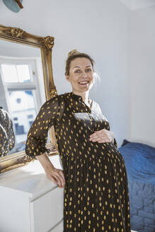 Porträt einer schwangeren Frau, die sich zu Hause an die Kommode lehnt - MFF05111