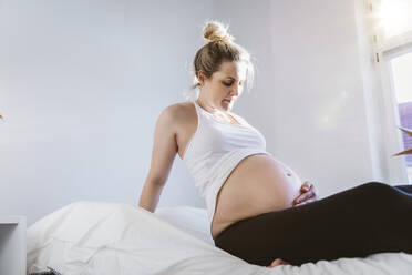 Schwangere Frau sitzt zu Hause auf dem Bett - MFF05117