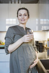 Porträt einer schwangeren Frau mit einem Glas Wasser in der Küche zu Hause - MFF05120