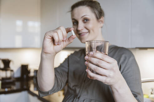 Porträt einer Frau mit Pille und Glas Wasser in der Küche zu Hause - MFF05121