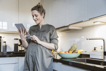 Schwangere Frau benutzt Tablet in der Küche zu Hause - MFF05124