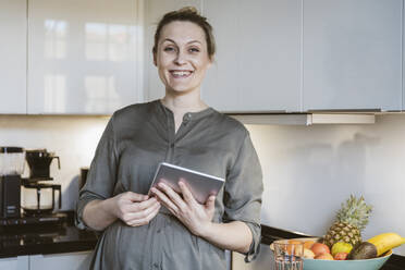 Porträt einer glücklichen schwangeren Frau mit einem Tablet in der Küche zu Hause - MFF05125