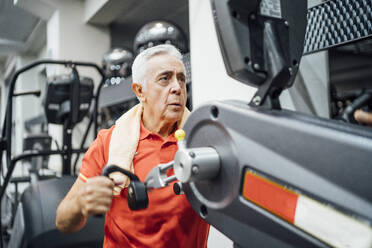 Senior man practising at exercise machine in gym - OCMF01093