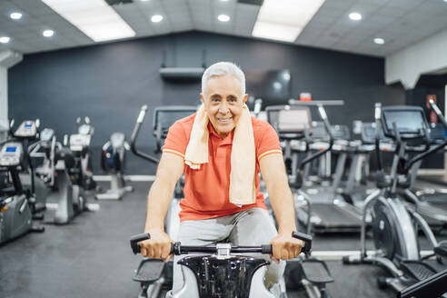 Porträt eines lächelnden älteren Mannes, der an einem Trainingsgerät im Fitnessstudio übt - OCMF01102