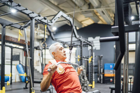 Älterer Mann übt an einer Kabelmaschine im Fitnessstudio, lizenzfreies Stockfoto