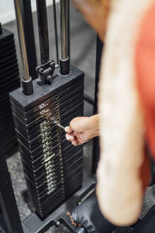 Close-up of man in gym setting weight of exercise machine - OCMF01106