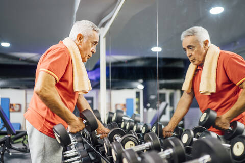 Älterer Mann nimmt Hanteln von der Ablage im Fitnessstudio, lizenzfreies Stockfoto