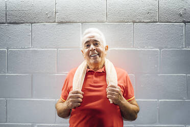 Porträt eines lächelnden älteren Mannes, der eine Pause macht und sich in einer Turnhalle an eine Wand lehnt - OCMF01112