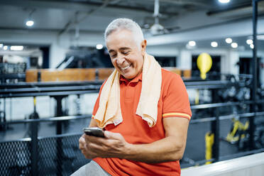 Happy senior man having a break and using cell phone in gym - OCMF01118