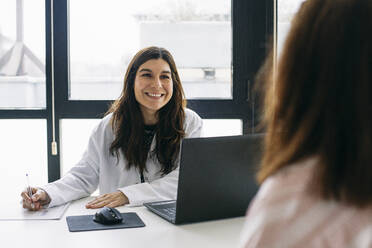 Lächelnder Arzt im Gespräch mit einem Patienten in einer Arztpraxis - ABZF02995