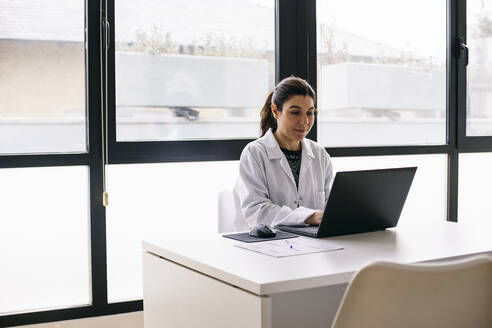 Arzt sitzt am Schreibtisch in einer Arztpraxis und benutzt einen Laptop - ABZF03013