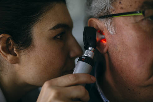 ENT physician examining ear of a senior man with an otoscope - ABZF03031