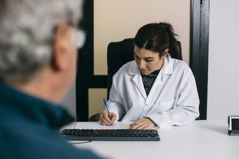 Arzt macht sich Notizen während einer Konsultation in einer Arztpraxis - ABZF03033