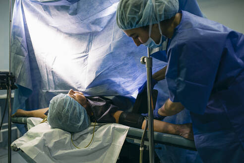 Anästhesist legt einem Patienten im Operationssaal eine Blutdruckmanschette an - ABZF03042