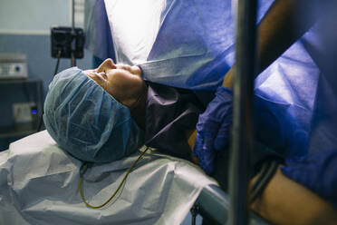 Anesthetist applying blood pressure cuff to patient in operating room - ABZF03043