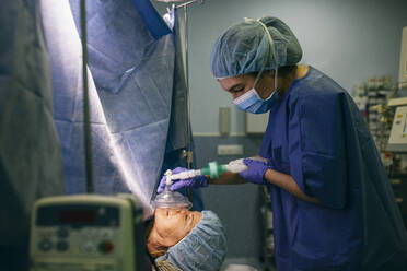 Anesthetist applying anesthesia machine to patient in operating room - ABZF03046